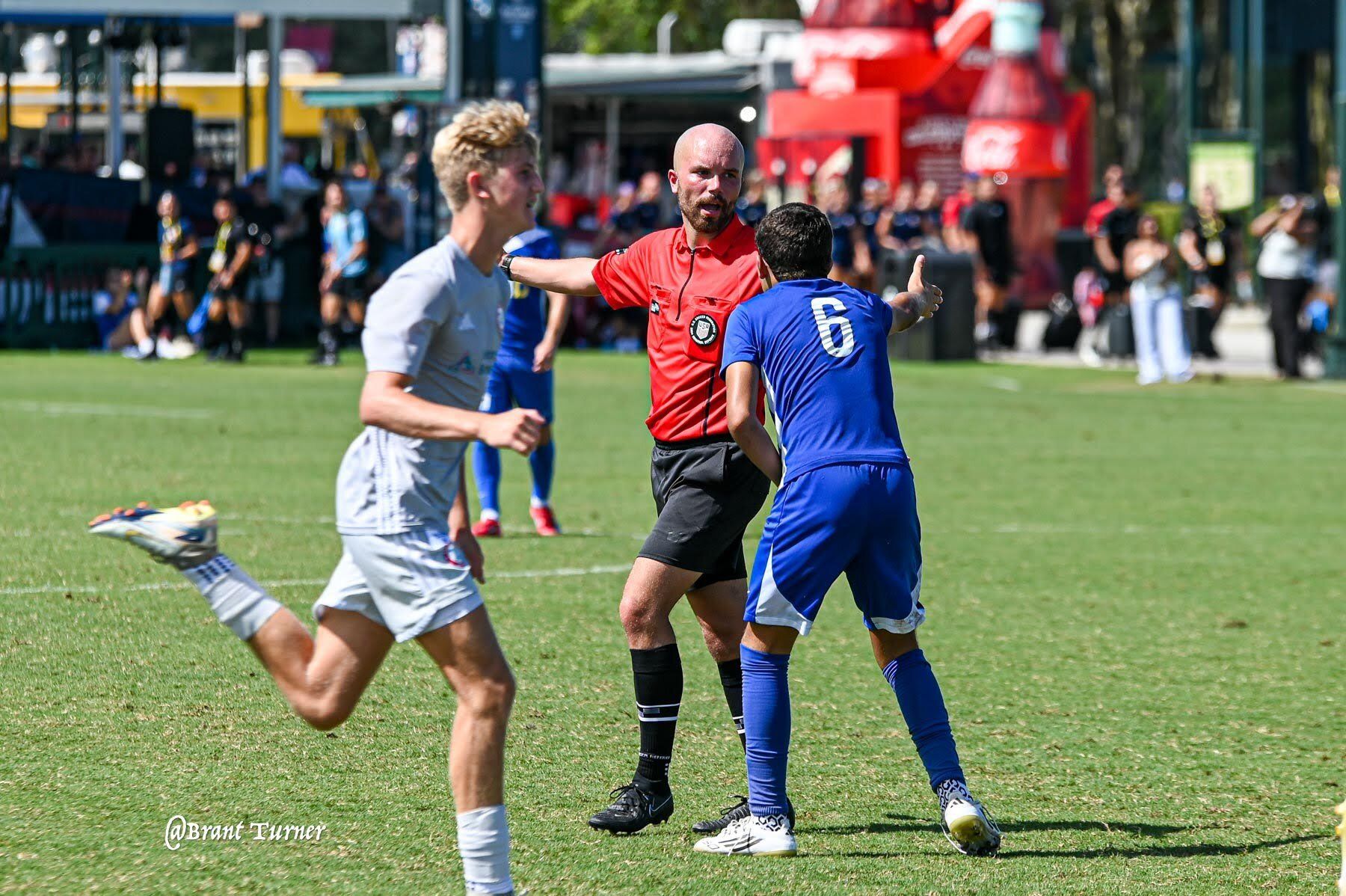 A referee speaking with soccer players on the field